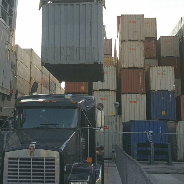 A large truck driving down the road near many stacks of containers.